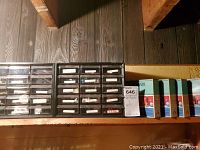 Two multi-drawer black plastic storage containers filled with various small hardware items, each drawer labeled, placed on a wooden surface.
