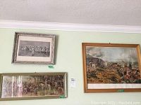 Three framed military prints displayed on a wall including a long horizontal print underneath two rectangular prints above.