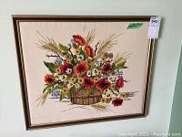 Full view of the framed vintage needlepoint artwork showing a colorful floral arrangement with wheat stalks in a basket on beige canvas.
