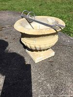 Concrete planter with the two metal spike holders resting inside it on a paved surface with grass in the background.