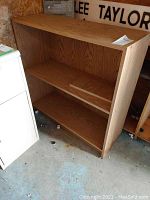 Front view of wooden shelf unit showing two shelves and wood grain finish. Visible scratches and wear.