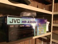 Photo showing the sealed JVC HR-A592U VCR box with model information and logos like VHS, SQPB, and NTSC.