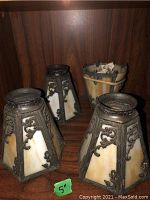 Four vintage glass and metal light shades displayed on wooden surface; three matching shades with ornate metal frames and yellowish-white glass panes, one damaged shade with broken glass and rubber bands