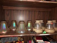 Shelf displaying eight glass lamp shades: six iridescent and two beige with bases