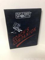 Closed black folder with Play It Again Sports logo and 'Coach's Companion' text with hockey player graphic