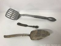 Photo showing the three serving utensils arranged side by side on a white surface with clear view of their handles and functional ends.