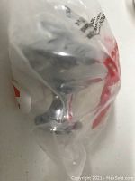 Close up of single chrome metal knob inside clear plastic packaging, showing hardware design and finish.