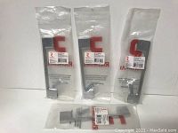 Four brand new metal contemporary pulls in original plastic packaging with Richelieu labels, displayed upright on a flat surface.