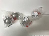 Four brushed nickel metal knobs individually packaged in clear plastic bags.