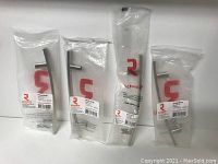 Four packaged metal cabinet pulls in polished nickel finish, each pull individually wrapped with visible Richelieu labels and screws inside packaging.