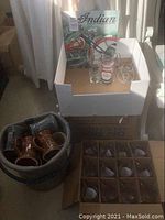 Wide view of the entire barware lot including glassware, ceramic steins in bucket, and motorcycle tin picture.