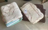 Photo showing a folded floral patterned quilt with scalloped edges next to a folded fuzzy brown blanket