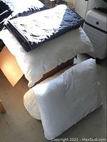 White pillows, one bolster style, with dark quilted bedding on top representing pillows and duvet included.