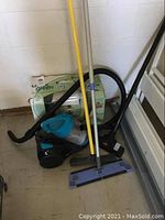 Wide view of Bissell Little Green Machine box behind Bissell PowerForce vacuum with mop leaning beside.