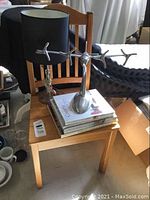 Wooden chair with black lamp resting on seat along with decorative styling books and silver metal airplane lamp base.