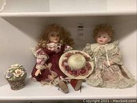 Three collector dolls with ceramic faces, lace-trimmed floral dresses, a ceramic floral basket, and a ceramic hat with fabric flowers shown together.