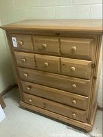 Front view of tall boy dresser showing all five drawers with round wooden knobs and wood grain finish.
