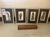 Set of four framed black and white Indigenous art prints and one wooden incense box on floor against a wall.