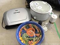 George Foreman Grill, Hamilton Beach Slow Cooker, decorative bowl, and electric pepper mill grouped together on floor.