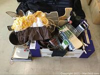 Box containing various kitchen utensils including graters, peelers, spatulas, apron, and other cooking tools.