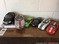 Wide view of six Motor Max model cars on a wooden surface against a white wall, showing various styles and colors, with a Classic Cars book beneath them.