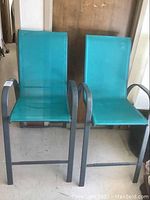Two turquoise mesh fabric outdoor bar chairs with metal frames positioned side by side.
