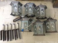 Six metal hexagonal hanging lanterns with etched glass hummingbird designs, shown with six matching hanging brackets and mounting hardware, all laid out on a surface.