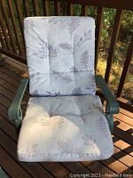 Close-up of one patio chair showing light gray cushions with leaf patterns, green metal frame with armrests