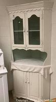 Full view of refurbished white farmhouse style corner hutch in two pieces with open scalloped middle section and glass doors on top.