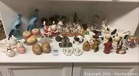 Wide shot of entire salt and pepper shaker collection showing various shaped ceramic, glass, and metal items arranged on a white surface.