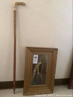 Overview photo of both the framed print and wood walking cane leaning against wall.