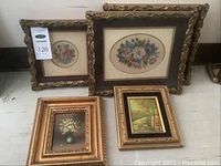 All five framed pictures together: two oval floral needlepoints with ornate gold frames, one dark framed floral needlepoint, and two small gold framed paintings.