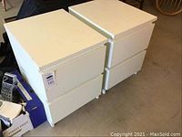 Pair of white two-drawer nightstands side by side, showing front and top surfaces with flat drawer fronts and simple modern style.