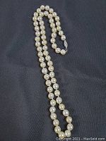 Full-length view of the pearl necklace laid on dark fabric