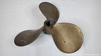 Close-up of the antique bronze boat propeller showing its three blades, central hub with keyway slot, and signs of age wear and patina.