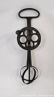 Front view of antique iron hand crank egg beater with circular gear and handle.