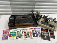Photo showing Atari CX-2600 console with nine game cartridges lined up, two joysticks, two paddles, manuals, and cords.