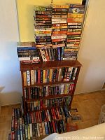 Wide view of the extensive book lot arranged on a bookshelf and on floor showing variety of titles and authors mainly thrillers and mysteries.