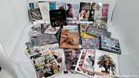 Overview of craft books and supplies including books on knitting, quilting, beading, floral arrangement, origami, and assorted beads and needles arranged on a white surface.
