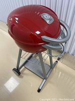 Red kettle-style electric grill on metal stand with wheels and lower shelf