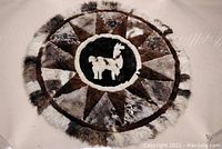 Top view of round lama alpaca fur rug showing central lama figure and multi-tone triangular patchwork pattern