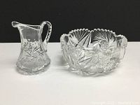Both the pinwheel crystal fruit bowl and pitcher side by side on white surface showing full set.