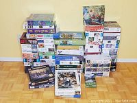 Multiple stacked boxed jigsaw puzzles showing assorted brands and piece counts