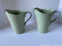 Two light green porcelain pitchers with wave texture, photographed from different angles to show sides, spouts, and handles.