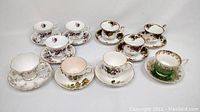 Overview of all 7 teacups and corresponding saucers, showing various floral designs and gold trim.