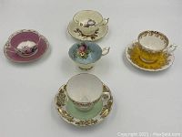 Five tea cups and saucers displayed together on white surface showing variety of colors and floral designs.