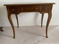 Full view of the vintage wooden desk showing its saber legs and three drawers with round metal knobs.