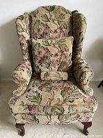 Front view of the wingback chair showing floral upholstery, seat cushion, and one decorative pillow.