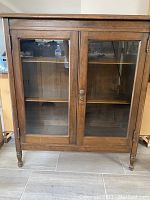 Front view of solid wood cabinet showing glass doors and turned legs
