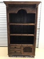 Front view of the tall hand carved wood cabinet with three shelves, three drawers, and a slatted lower cabinet door.